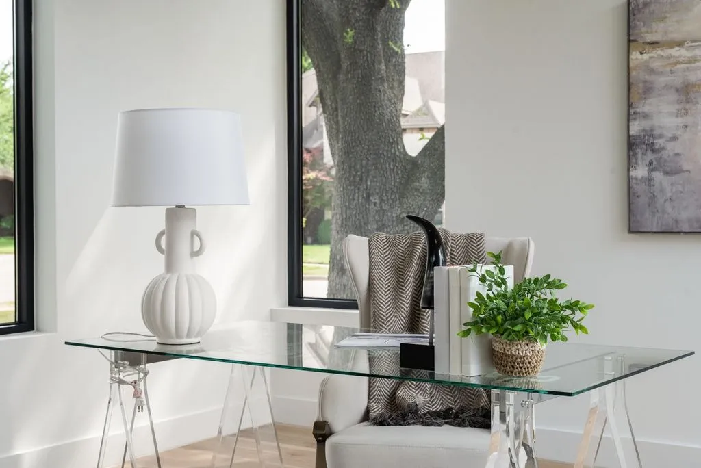 Glass desk with a lamp beside a window
