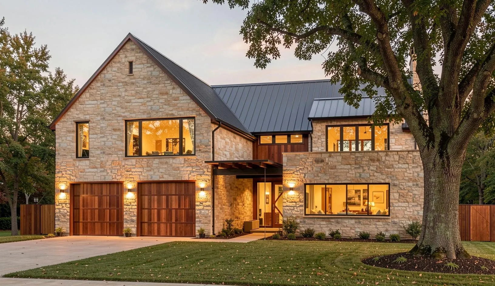 Concept rendering of the planned home: stone walls, a dark metal roof and wood garage doors behind a large oak